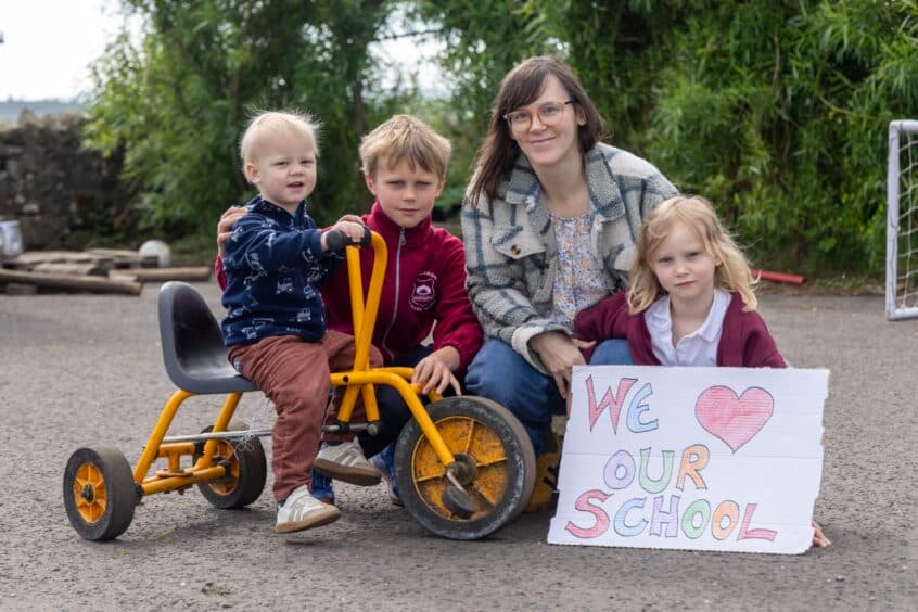 A Logiealmond family holding a hand-made “We love our school” sign